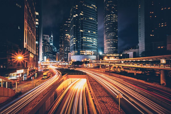 Street traffic in Hong Kong at night. Office skyscraper buildings and busy traffic on highway road with blurred cars light trails. Hong Kong