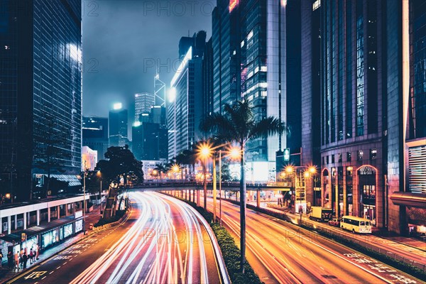 Street traffic in Hong Kong at night. Office skyscraper buildings and busy traffic on highway road with blurred cars light trails. Hong Kong