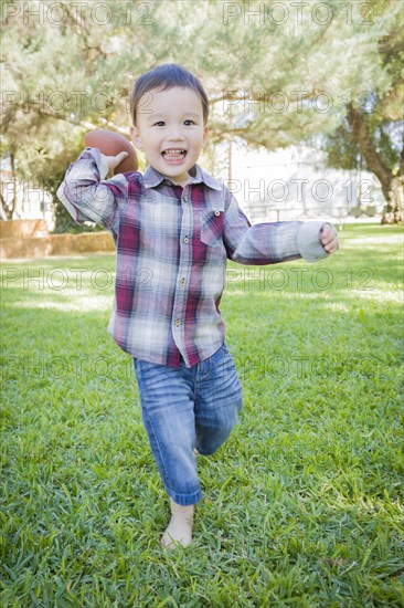 Cute young mixed-race boy playing football outside at the park