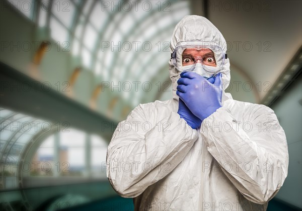 Man covering mouth with hands wearing HAZMAT protective clothing inside building