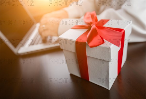 White gift box with red ribbon and bow near man typing on laptop computer