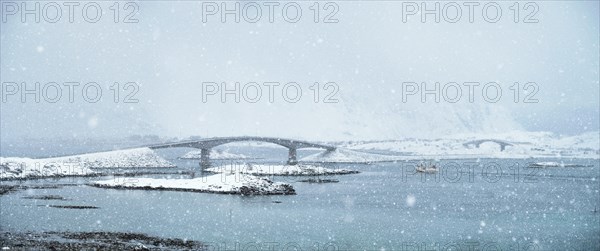 Fredvang bridges in heavy snowfall in winter with fishing ship. Lofoten islands