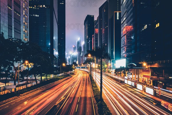 Street traffic in Hong Kong at night. Office skyscraper buildings and busy traffic on highway road with blurred cars light trails. Hong Kong