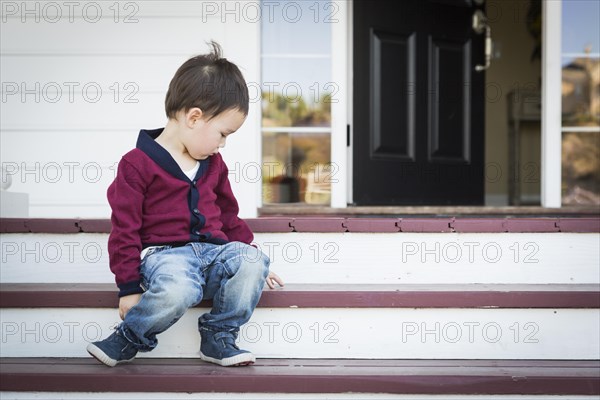 Cute melancholy mixed-race boy sitting on front porch steps