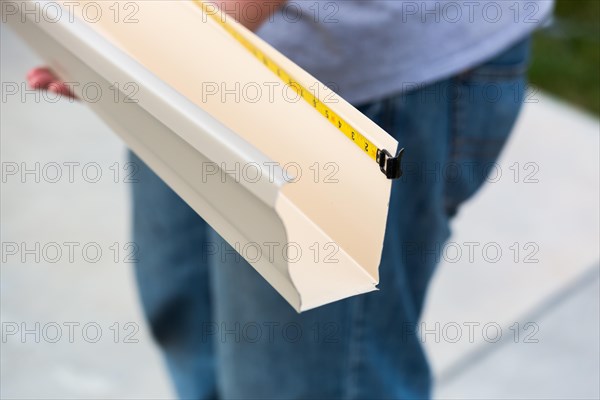 Worker measuring an aluminum rain gutter feeding through seamless shaping machine