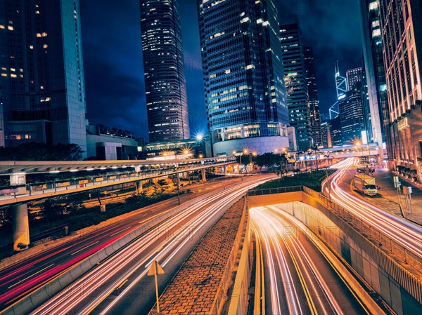 Street traffic in Hong Kong at night. Office skyscraper buildings and busy traffic on highway road with blurred cars light trails. Hong Kong