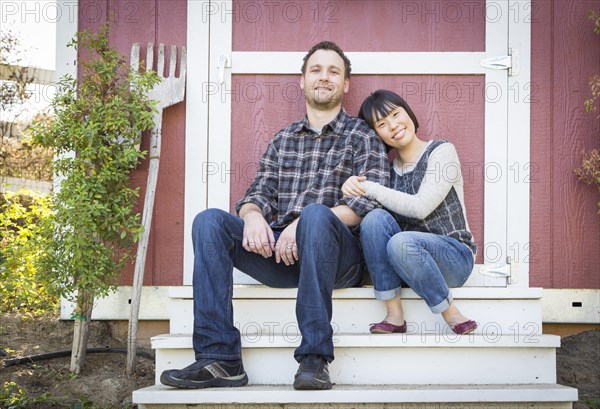 Happy mixed-race couple relaxing on the steps of their barn
