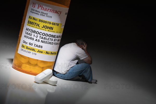 Man holding head sitting next to hydrocodeon pills and bottle