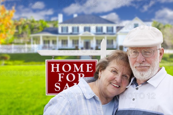 Happy senior couple front of for sale real estate sign and house