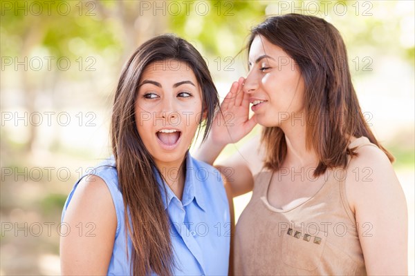 Two beautiful ethnic twin sisters whispering secrets outdoors