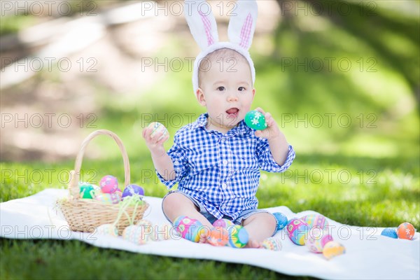 mixed-race chinese and caucasian baby boy outside wearing rabbit ears playing with easter eggs