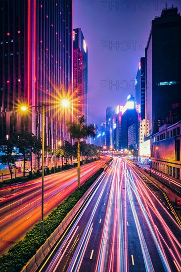 Street traffic in Hong Kong at night. Office skyscraper buildings and busy traffic on highway road with blurred cars light trails. Hong Kong