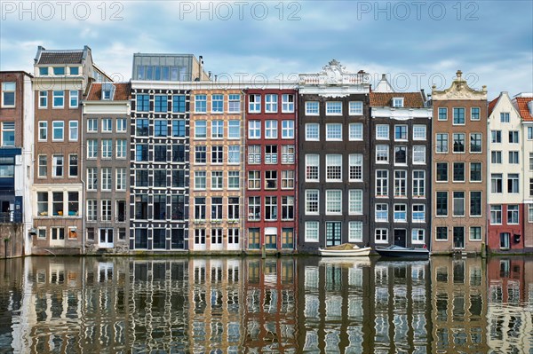 Row of typical houses and boat on Amsterdam canal Damrak with reflection. Amsterdam