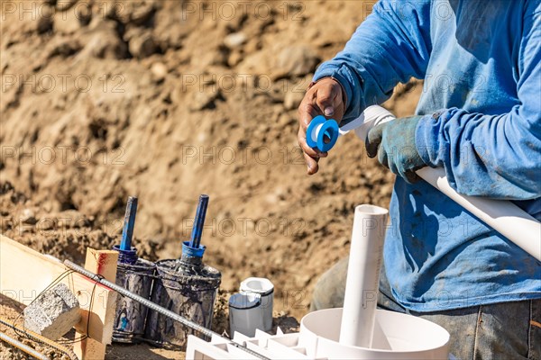 Plumber applying PTFE tape to PVC pipe at construction site