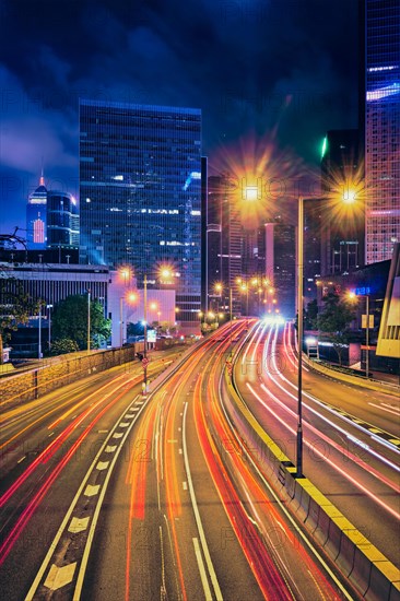 Street traffic in Hong Kong at night. Office skyscraper buildings and busy traffic on highway road with blurred cars light trails. Hong Kong