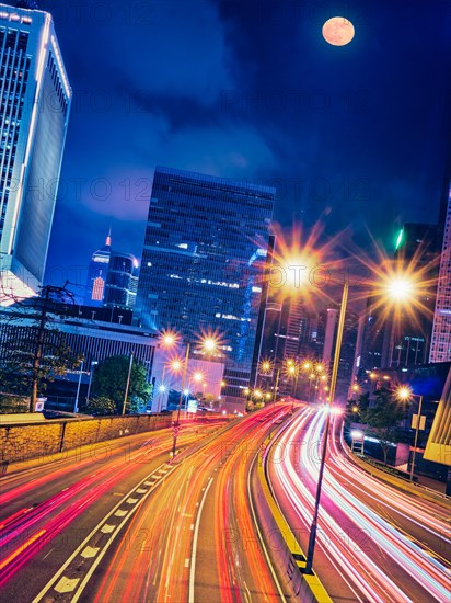 Street traffic in Hong Kong at night. Office skyscraper buildings and busy traffic on highway road with blurred cars light trails. Hong Kong