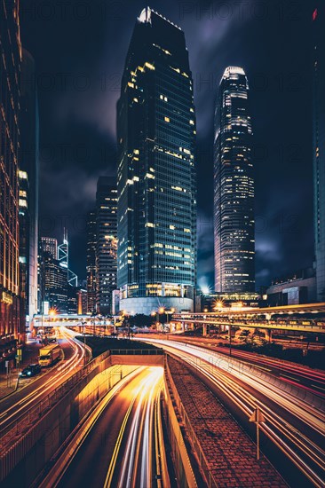 Street traffic in Hong Kong at night. Office skyscraper buildings and busy traffic on highway road with blurred cars light trails. Hong Kong