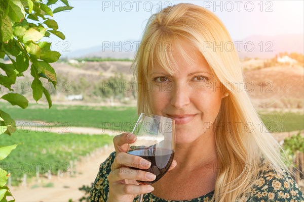 Beautiful young adult woman enjoying glass of wine tasting in the vineyard