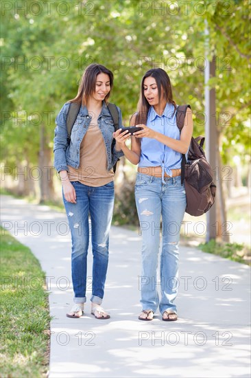 Two beautiful young ethnic twin sisters with backpacks using A smartphone outside