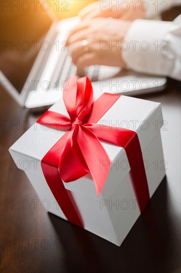 White gift box with red ribbon and bow near man typing on laptop computer