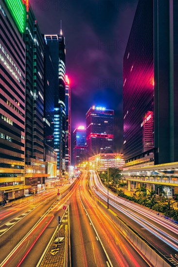 Street traffic in Hong Kong at night. Office skyscraper buildings and busy traffic on highway road with blurred cars light trails. Hong Kong