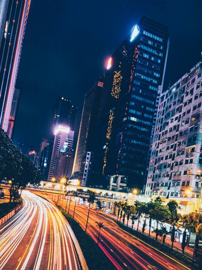 Street traffic in Hong Kong at night. Office skyscraper buildings and busy traffic on highway road with blurred cars light trails. Hong Kong