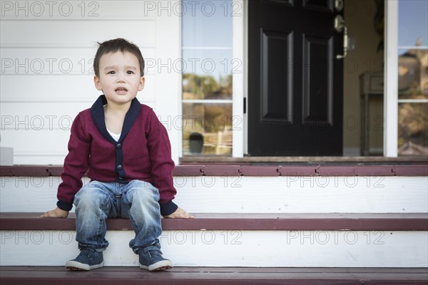 Cute melancholy mixed-race boy sitting on front porch steps