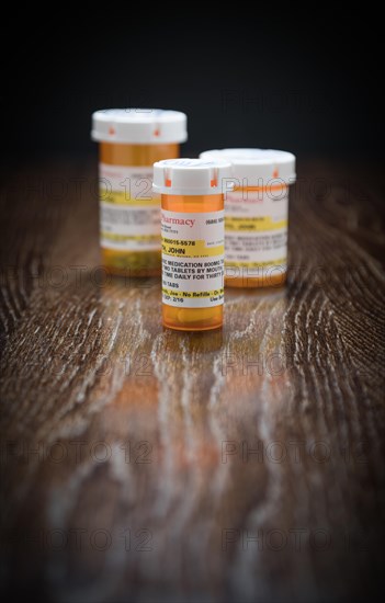 Variety of non-proprietary prescription medicine bottles on reflective wooden surface