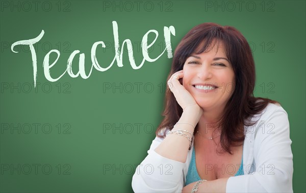 Teacher written on green chalkboard behind smiling middle aged woman