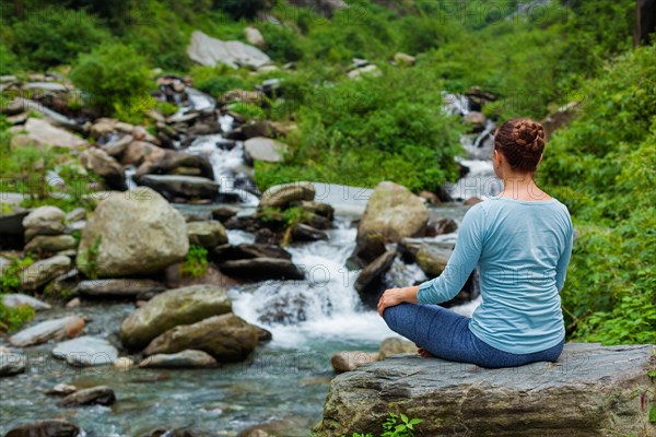 Woman in Hatha yoga asana Padmasana outdoors at tropical waterfall