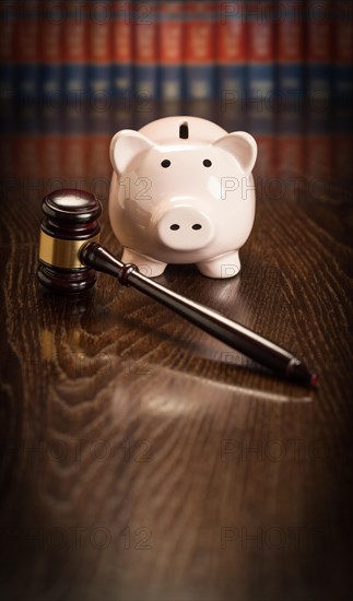 Gavel and piggy bank on wooden table with law books in background