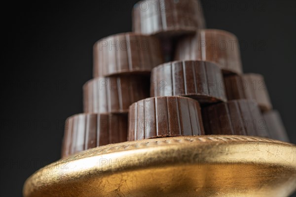 Stack of fine chocolates on golden pillar dish with dark background