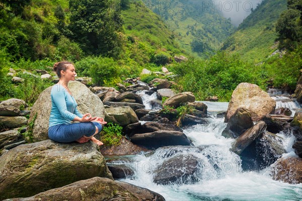 Woman in Hatha yoga asana Padmasana outdoors at tropical waterfall