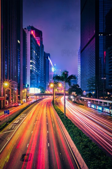 Street traffic in Hong Kong at night. Office skyscraper buildings and busy traffic on highway road with blurred cars light trails. Hong Kong