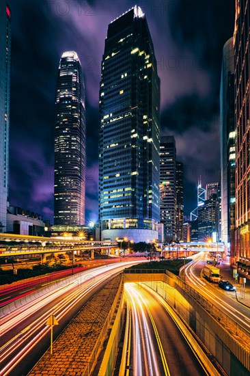 Street traffic in Hong Kong at night. Office skyscraper buildings and busy traffic on highway road with blurred cars light trails. Hong Kong