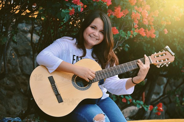 A girl sitting playing guitar outdoors