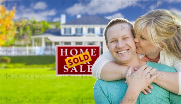 Happy couple hug in front of sold real estate sign and beautiful new house