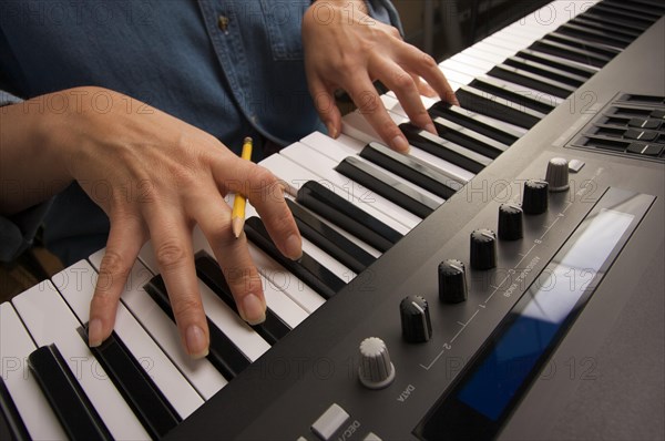 Woman's fingers with pencil on digital piano keys