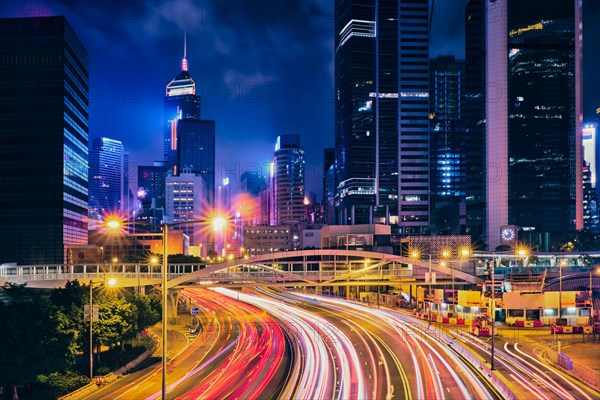 Street traffic in Hong Kong at night. Office skyscraper buildings and busy traffic on highway road with blurred cars light trails. Hong Kong