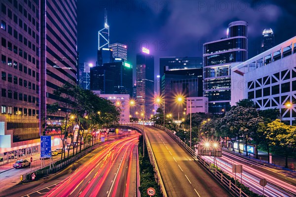 Street traffic in Hong Kong at night. Office skyscraper buildings and busy traffic on highway road with blurred cars light trails. Hong Kong