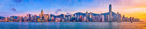 Panorama of Hong Kong skyline cityscape downtown skyscrapers over Victoria Harbour in the evening with junk tourist ferry boat on sunset with dramatic sky. Hong Kong