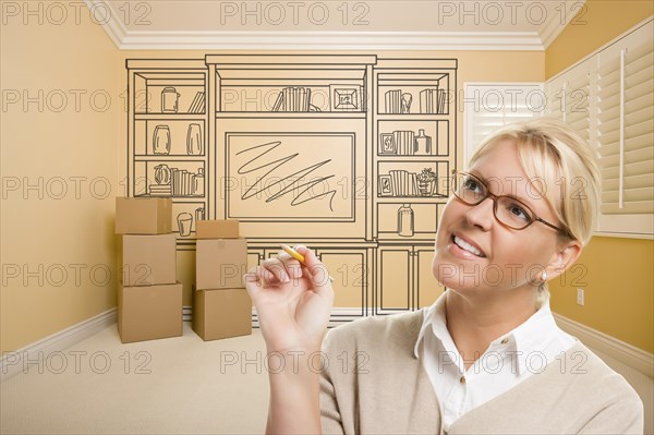 Female holding pencil in room with moving boxes and drawing of entertainment unit on wall