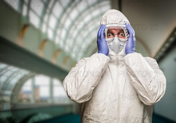 Man holding head with hands wearing HAZMAT protective clothing inside building