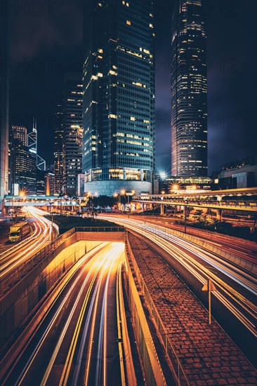 Street traffic in Hong Kong at night. Office skyscraper buildings and busy traffic on highway road with blurred cars light trails. Hong Kong