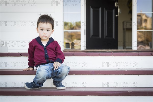 Cute melancholy mixed-race boy sitting on front porch steps