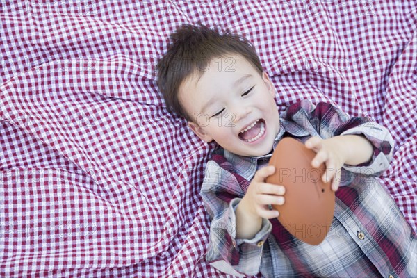 Cute young mixed-race boy playing with football outside on picnic blanket