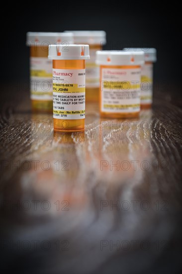 Variety of non-proprietary prescription medicine bottles on reflective wooden surface