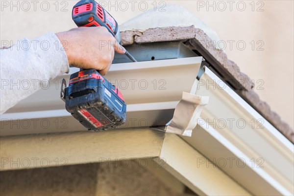 Worker attaching aluminum rain gutter to fascia of house