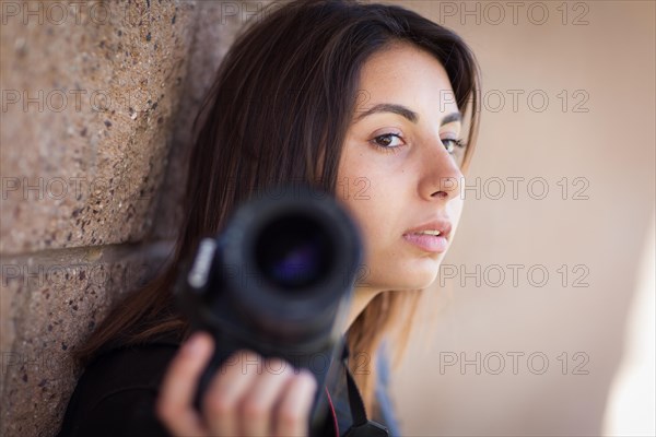 Young adult ethnic female photographer against wall holding camera