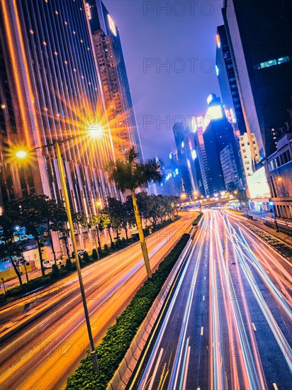 Street traffic in Hong Kong at night. Office skyscraper buildings and busy traffic on highway road with blurred cars light trails. Hong Kong